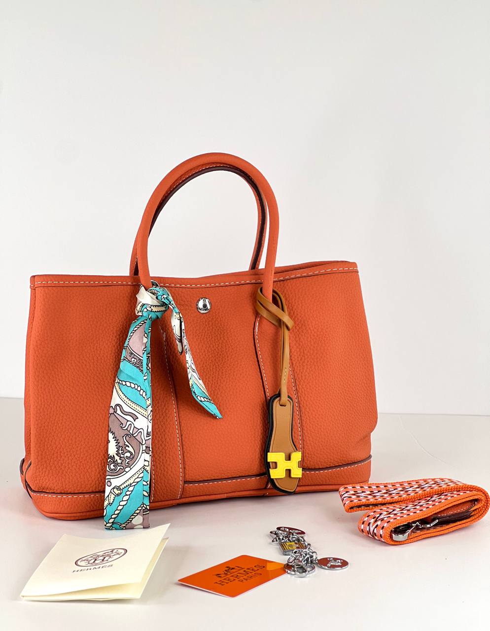 Orange handbag with scarf, tag, and pouch on a white background