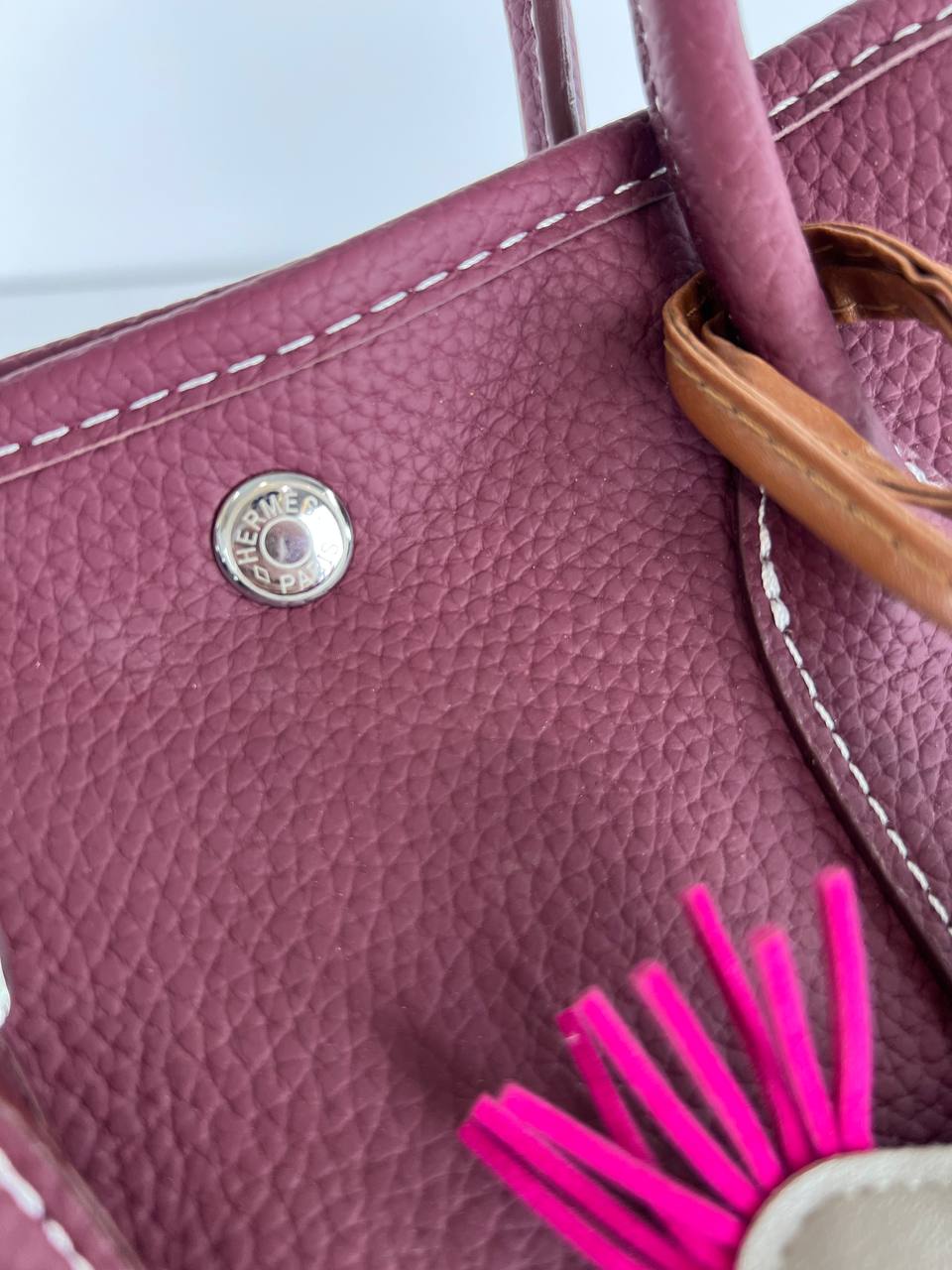 Close-up of a pink handbag with a brand logo and pink tassel on a light blue background