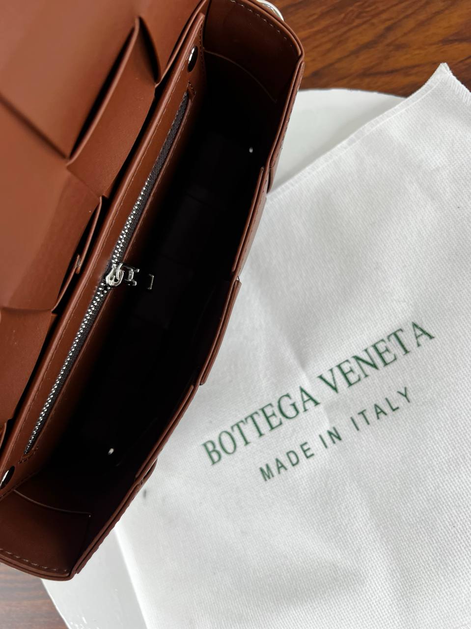 Brown leather handbag on a white Bottega Veneta dust bag with 'Made in Italy' text.