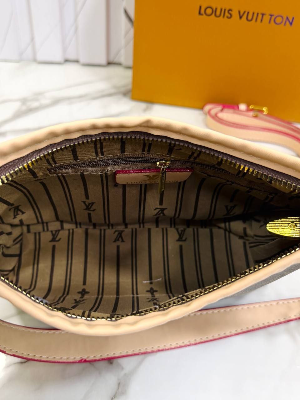Louis Vuitton handbag with open lid showing interior pattern, placed on a white surface.