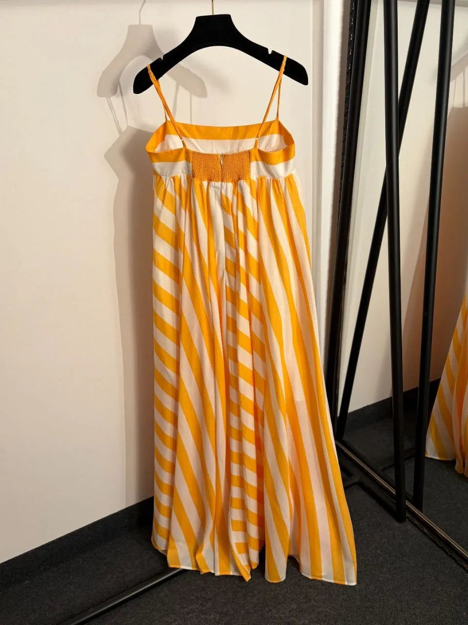 Yellow and white striped dress on a hanger against a neutral background
