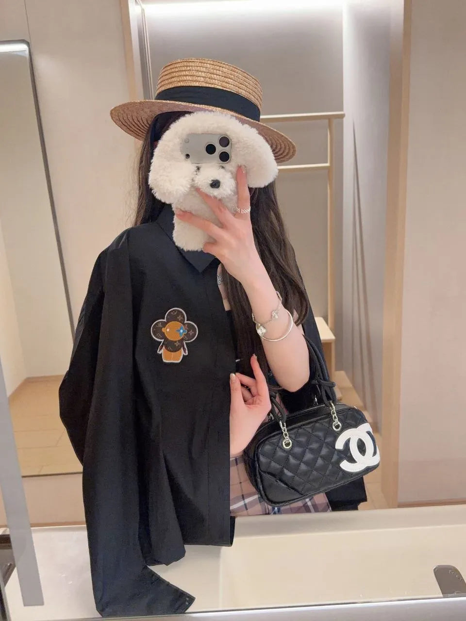Person holding a Chanel handbag in front of a mirror, wearing a black outfit with a floral design.