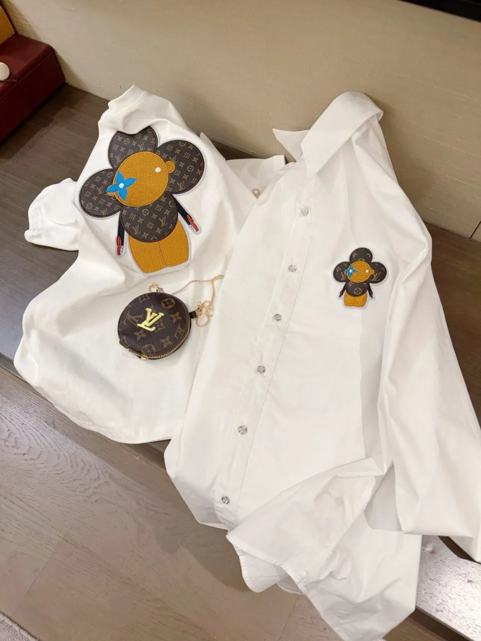 White shirt with cartoon bee design and Louis Vuitton bag on a wooden surface