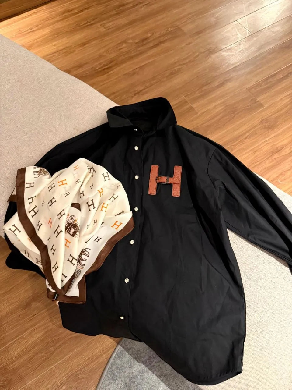 Black shirt with brown 'H' logo on a wooden floor