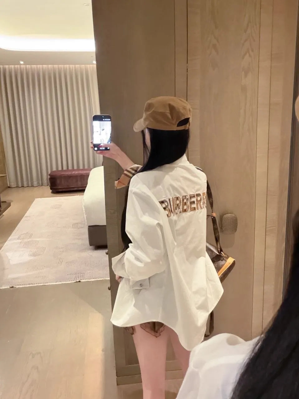 Person wearing a white jacket with 'BARBIERI' branding, taking a mirror selfie in a room.