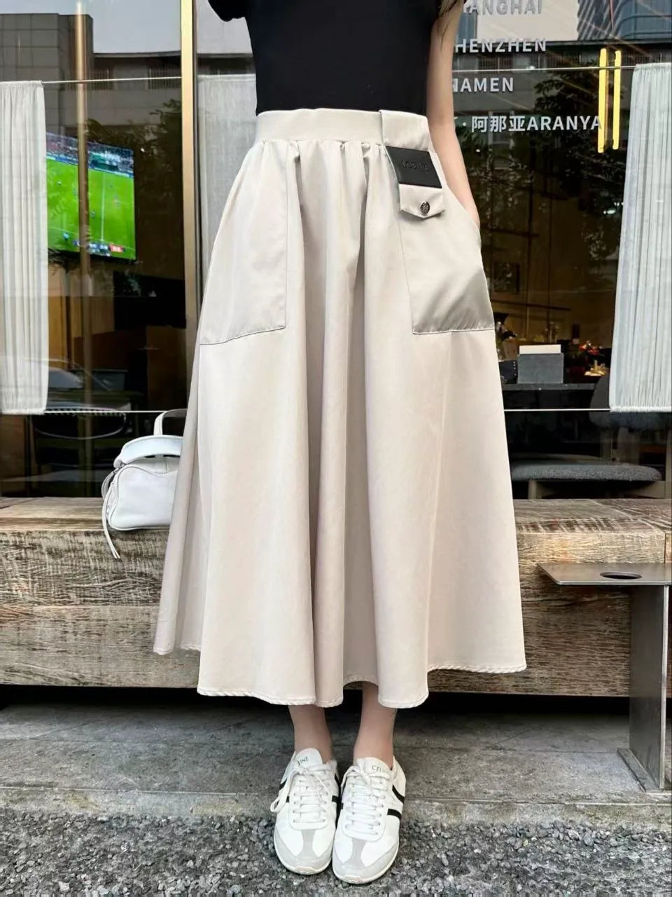 Person wearing a beige skirt with a black top and white shoes in front of a store.