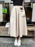 Person wearing a beige skirt with a black top and white shoes in front of a store.