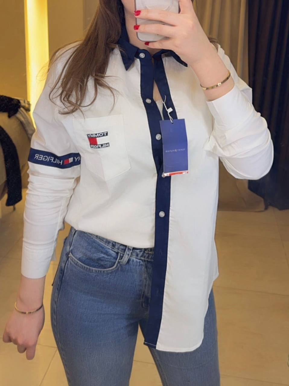 Female model wearing Tommy Hilfiger white relaxed fit shirt blue relaxed jeans white sneakers light gray studio background