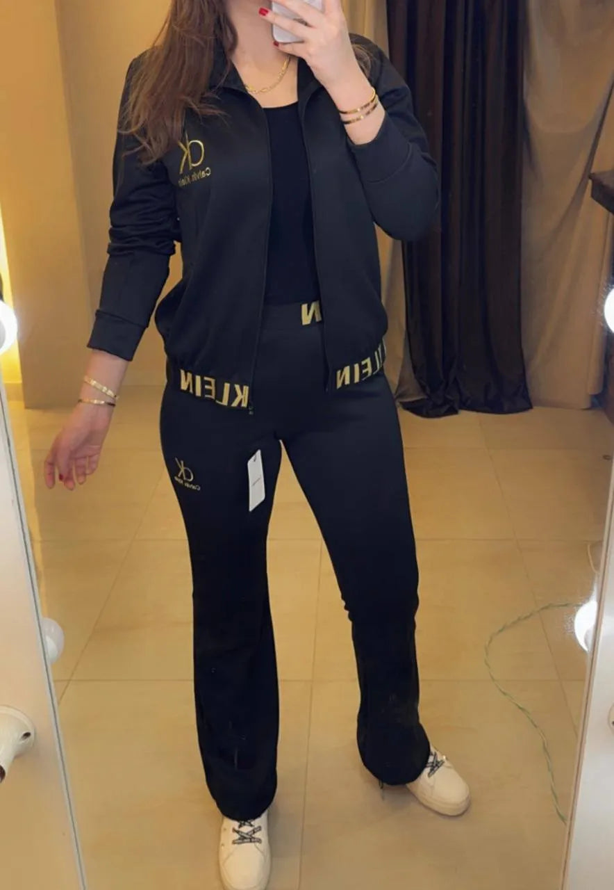 Female model wearing Calvin Klein black gold tracksuit set full body white sneakers studio background