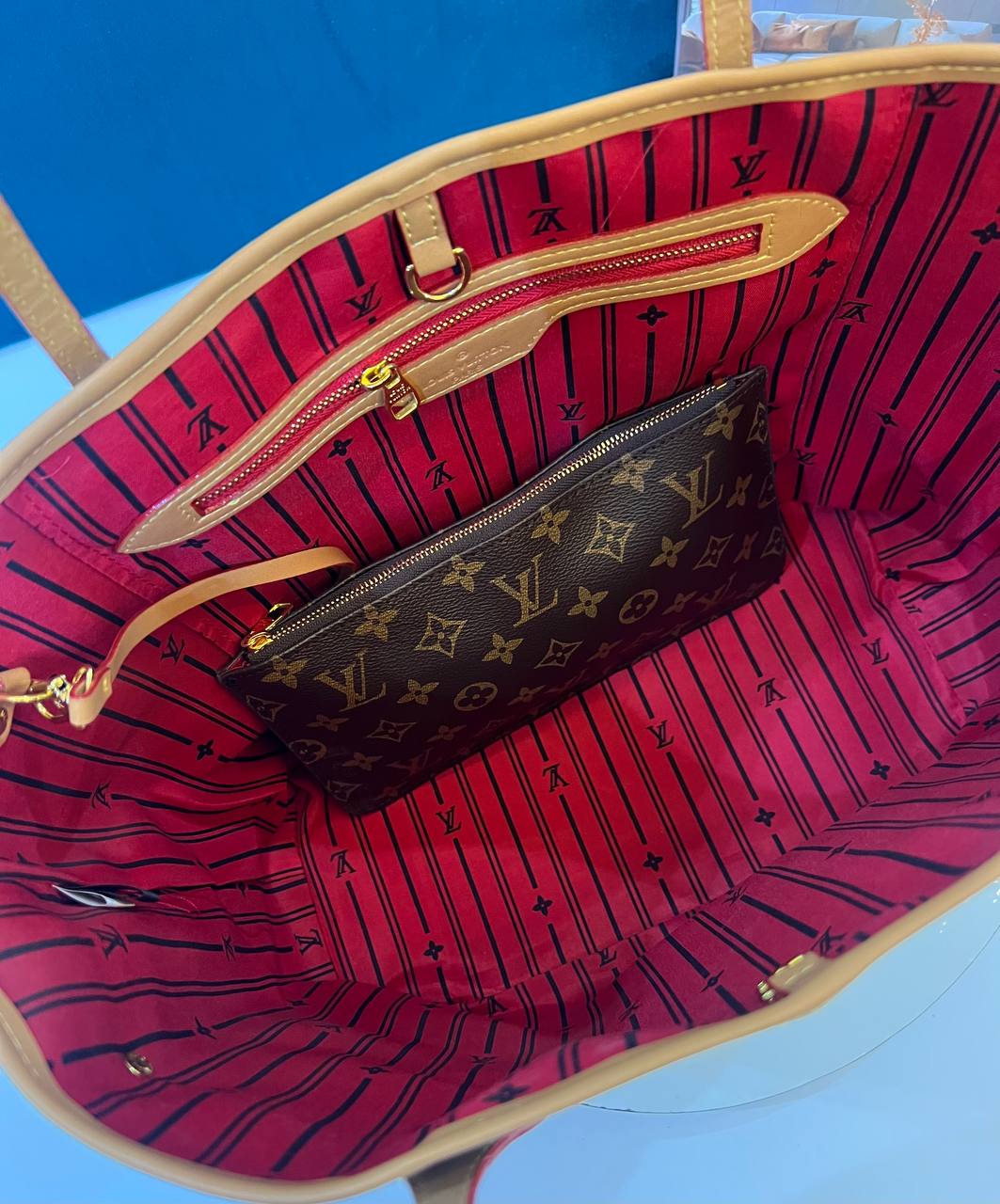Red patterned handbag with a smaller brown monogrammed bag inside, on a blue background.