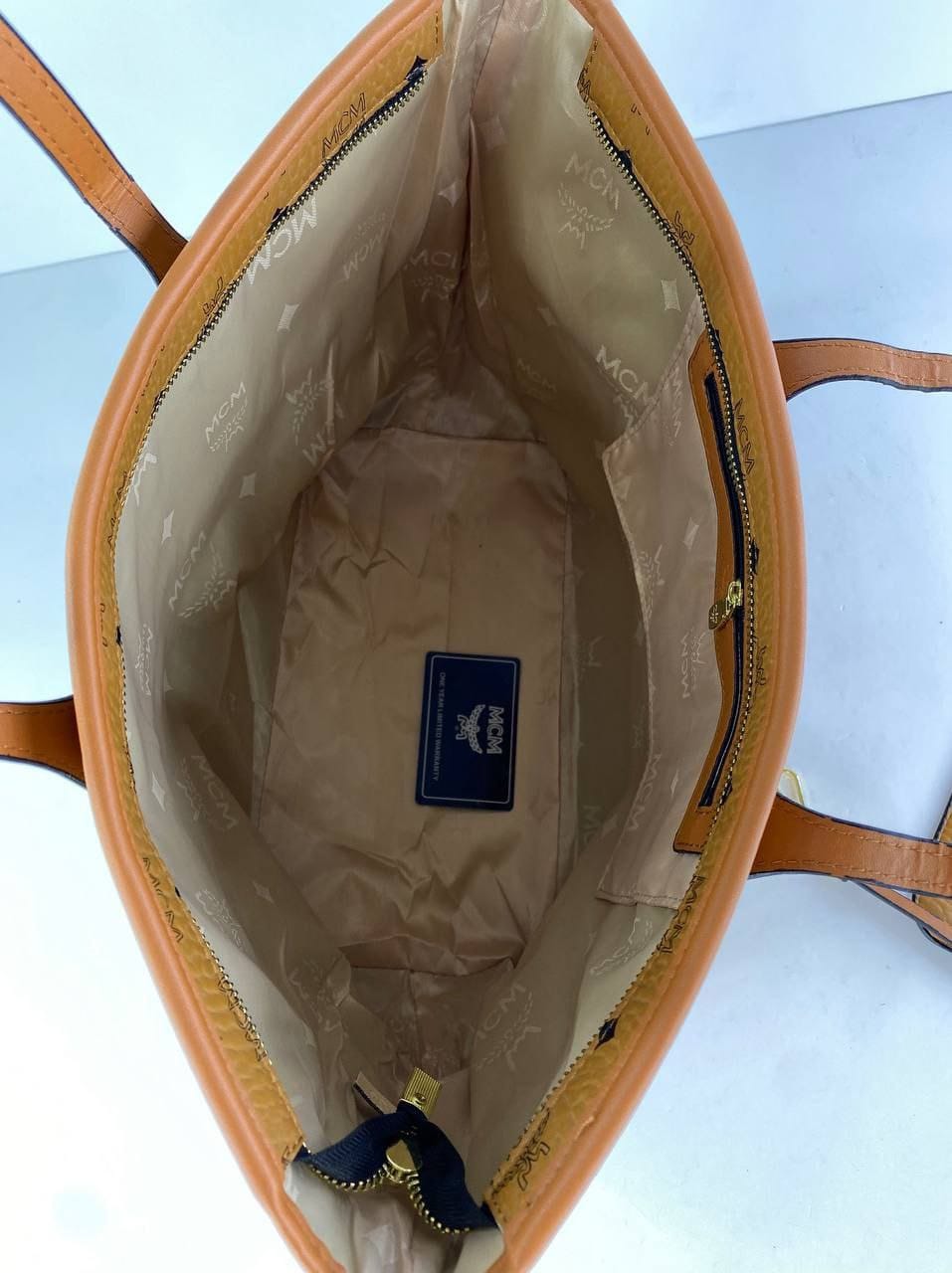 Open brown leather handbag with visible brand logo on a light blue background