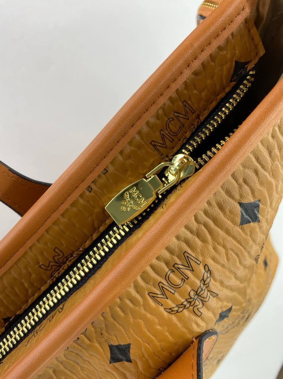 Close-up of a brown handbag with gold zipper and visible MCM logo.