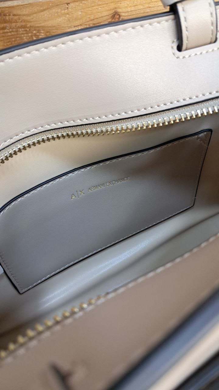 Close-up of a beige handbag with a visible brand name on a wooden surface.