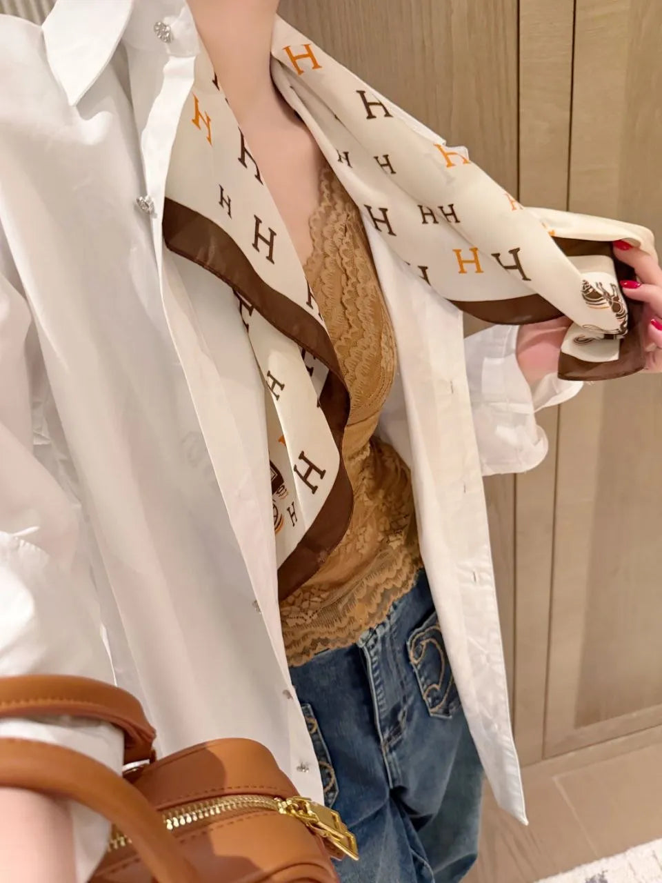 Person wearing a white shirt with a patterned scarf, holding a brown bag.