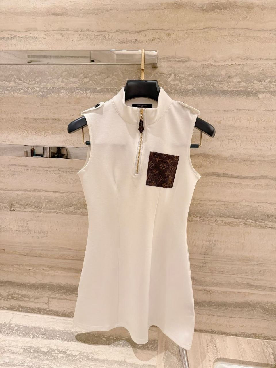 White sleeveless top with a brown patch on a hanger against a marble wall.