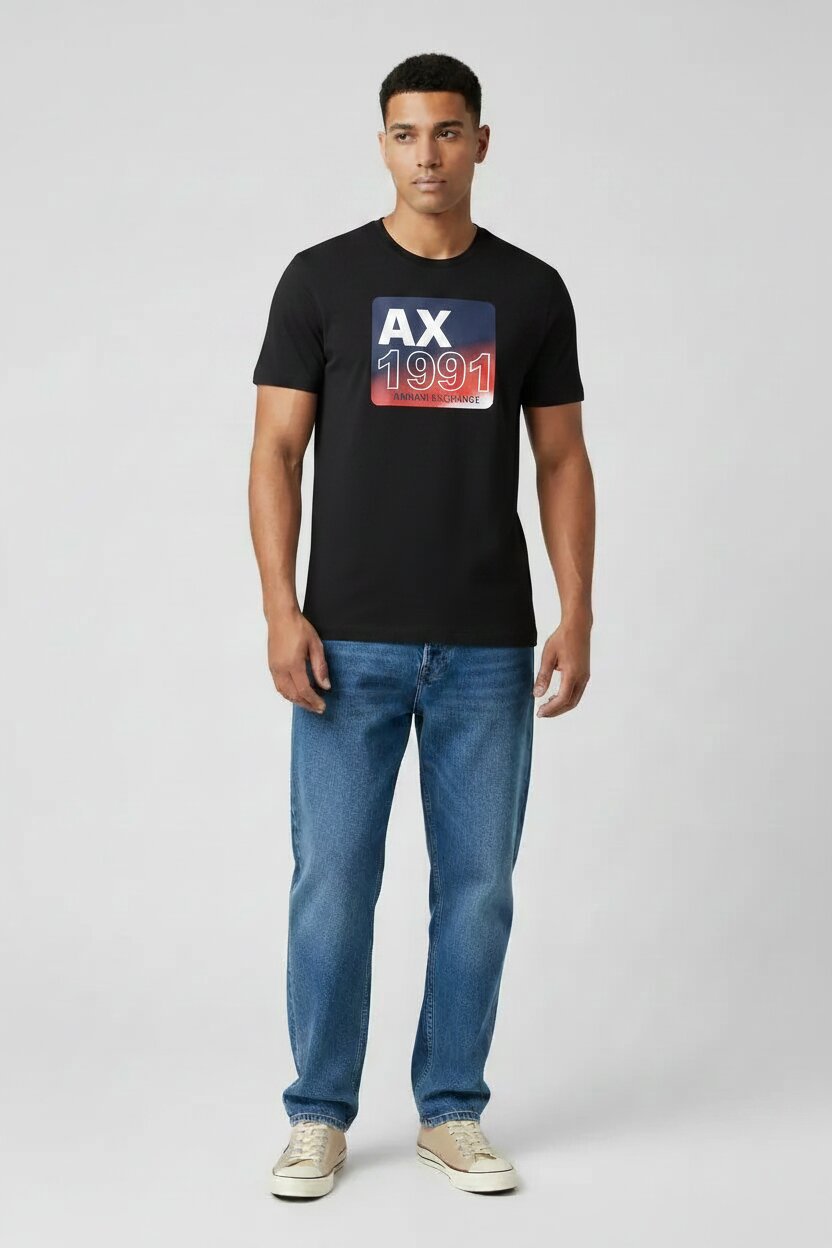 Armani Exchange Black AX 1991 Graphic T-Shirt on Male Model - Medium Blue Straight Leg Jeans and Beige Sneakers - Light Gray Studio Background - Full Body Shot