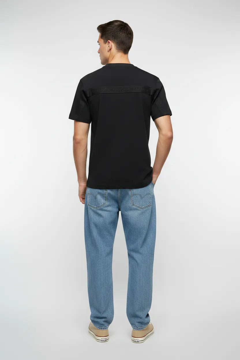 Male model wearing Armani Exchange black t-shirt back view with blue denim and beige sneakers