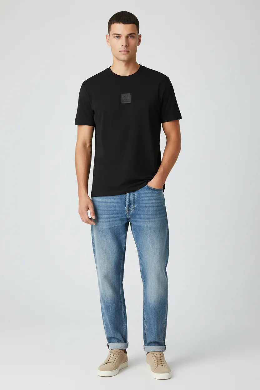Male model wearing Armani Exchange black t-shirt with loose fit jeans and beige sneakers front view