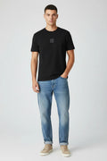 Male model wearing Armani Exchange black t-shirt with loose fit jeans and beige sneakers front view