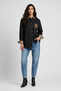 Woman wearing a black varsity jacket with a logo, blue jeans, and black boots on a white background