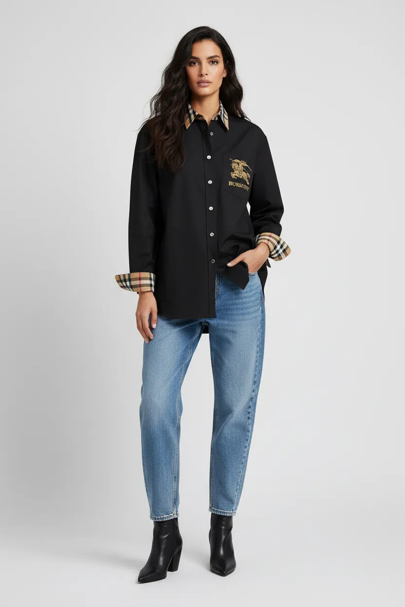 Woman wearing a black varsity jacket with a logo, blue jeans, and black boots on a white background