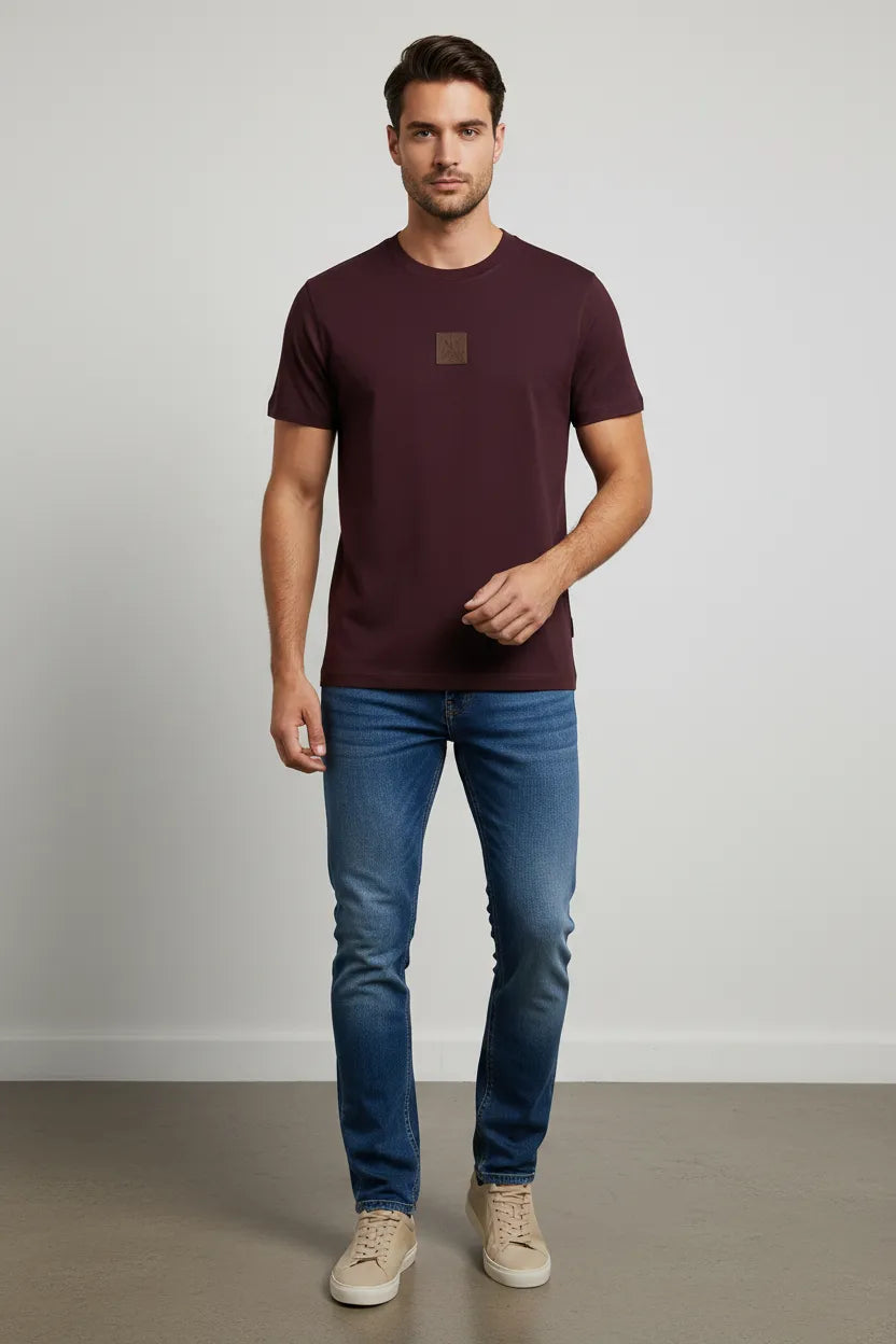 Man wearing a maroon t-shirt and blue jeans against a plain background
