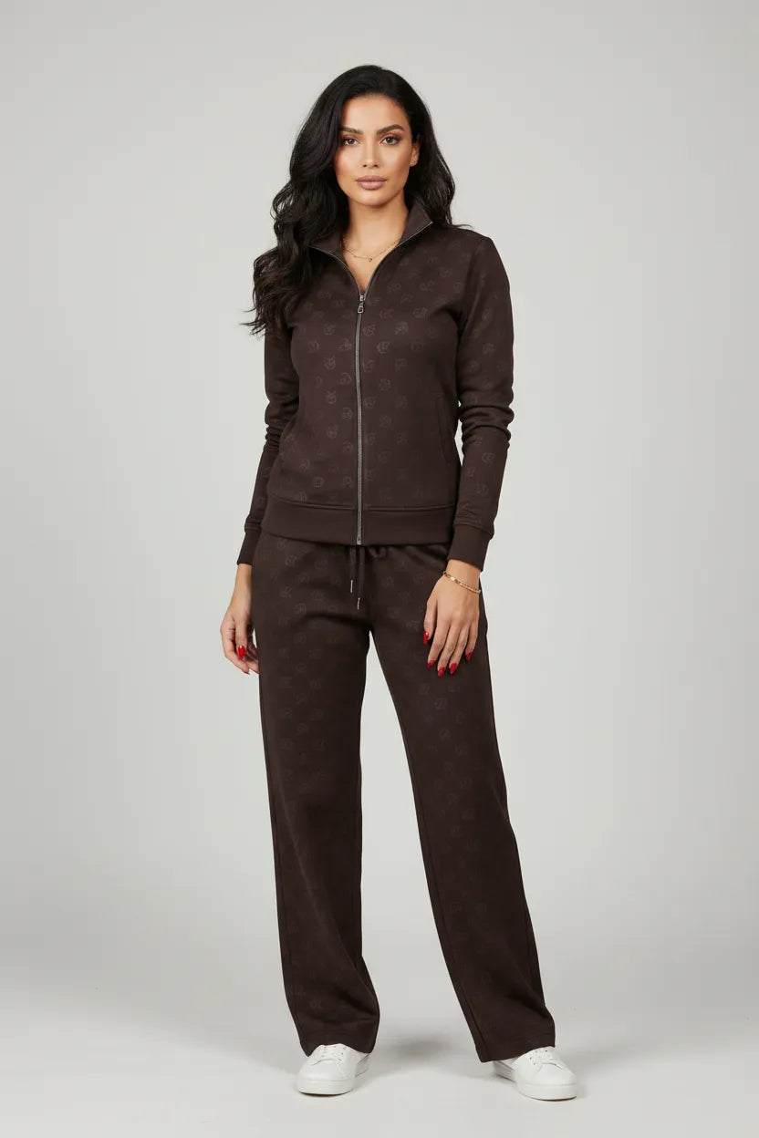 Female model wearing Calvin Klein CK monogram dark brown tracksuit set full body white sneakers gold accessories gray studio background