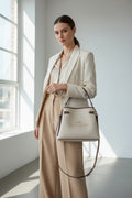 Woman in a beige suit holding a Coach handbag in a bright room.
