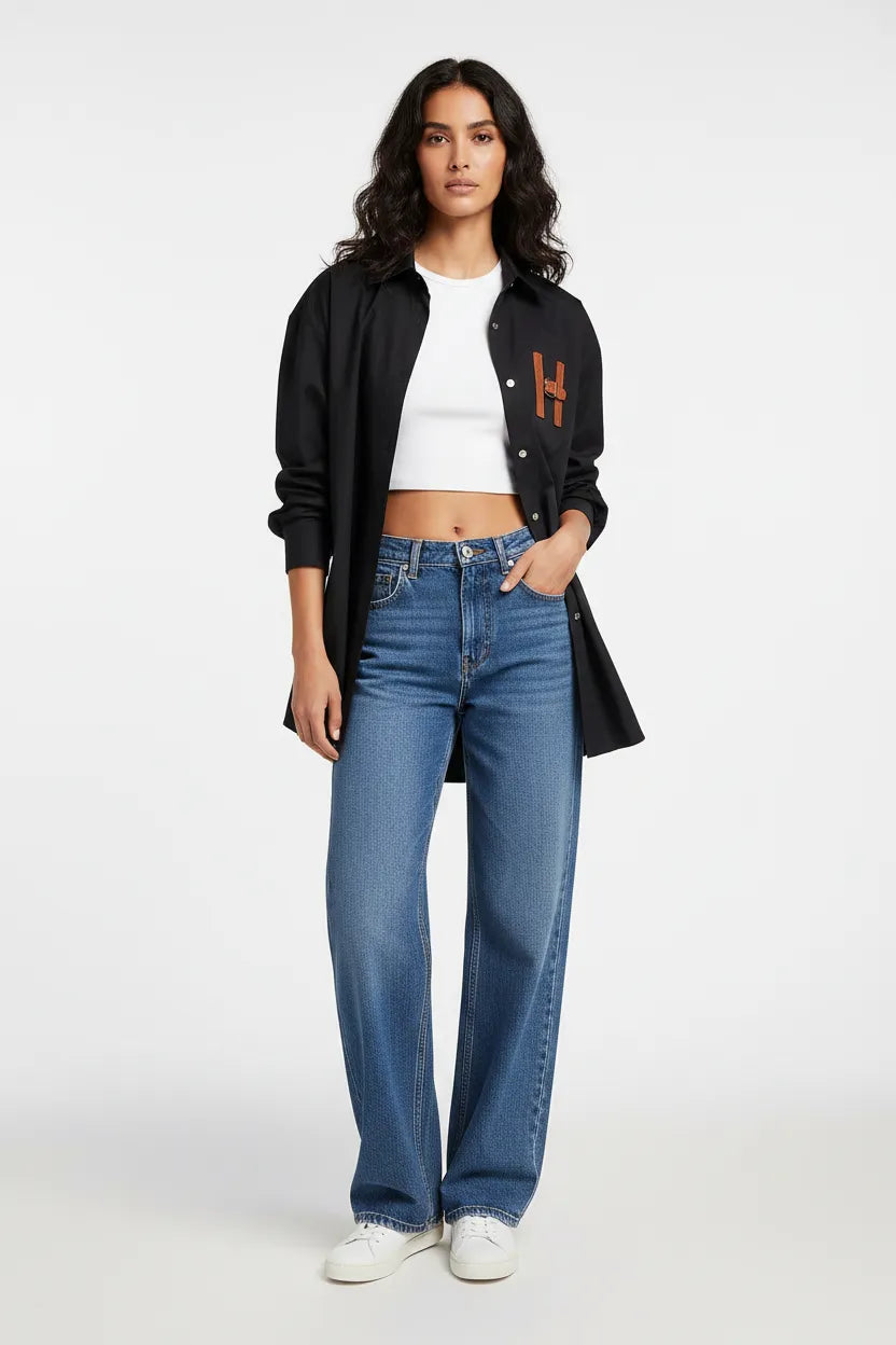 Woman wearing a black jacket with a logo, white shirt, and blue jeans on a white background