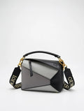 Gray and black handbag with gold accents on a light gray background