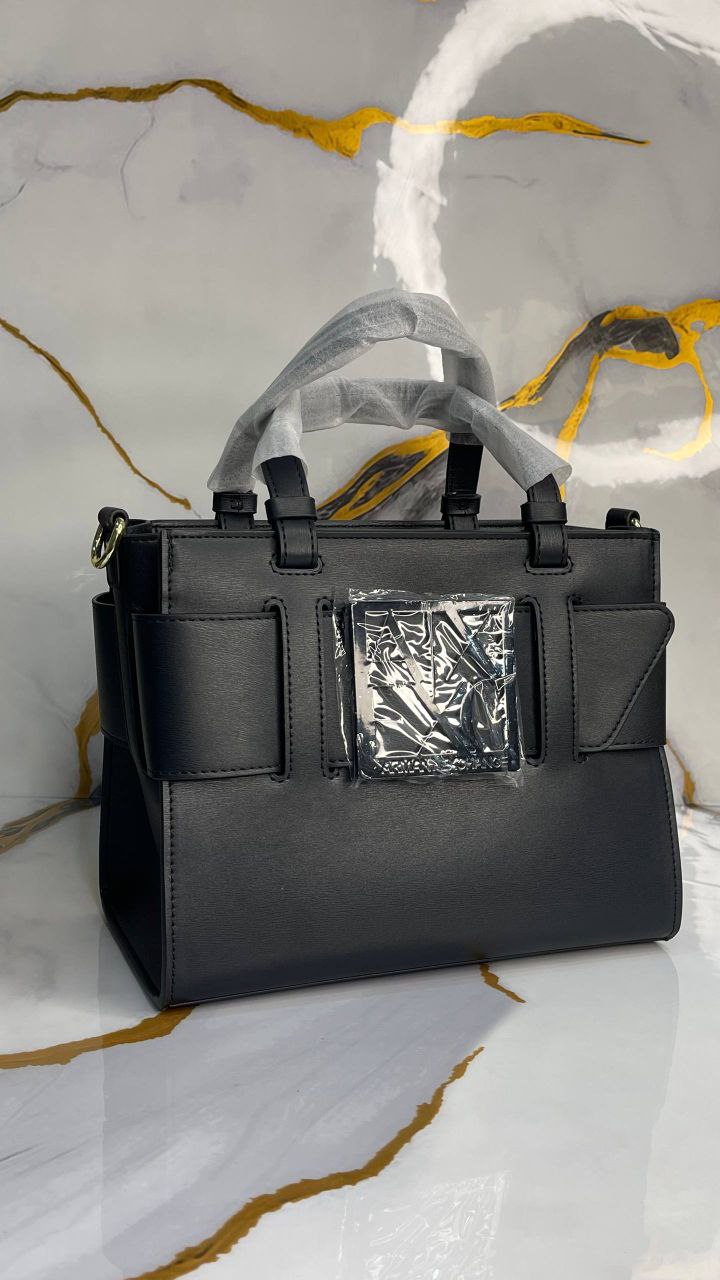 Black handbag with a reflective silver buckle on a marble surface