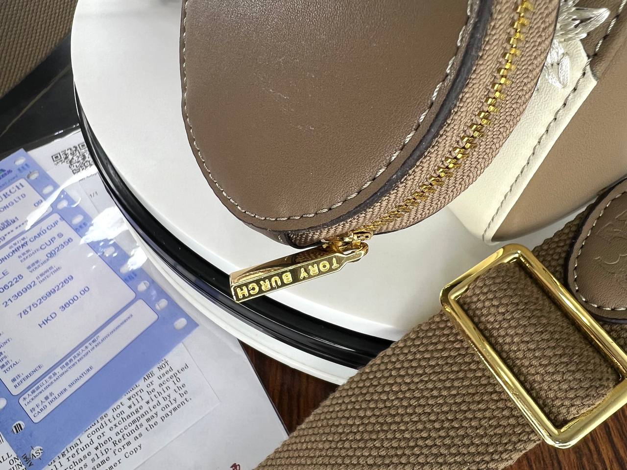 Close-up of a brown leather bag with gold zipper and strap on a white surface.