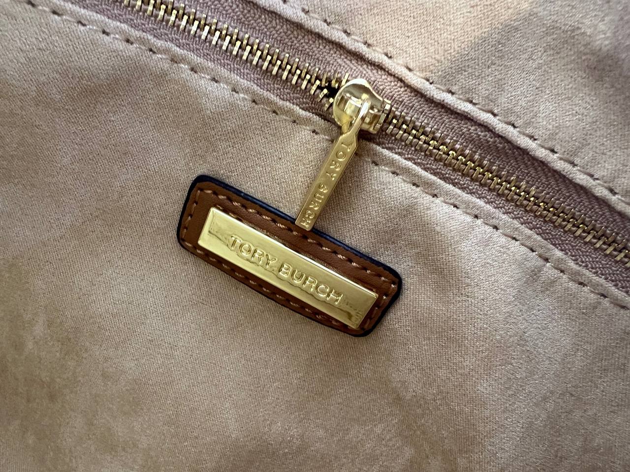 Close-up of a beige bag with a gold zipper and visible brand name tag.