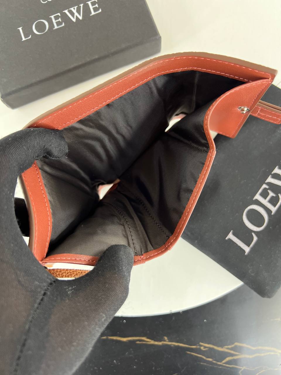 Close-up of a Loewe product with a black glove holding it, on a white background.