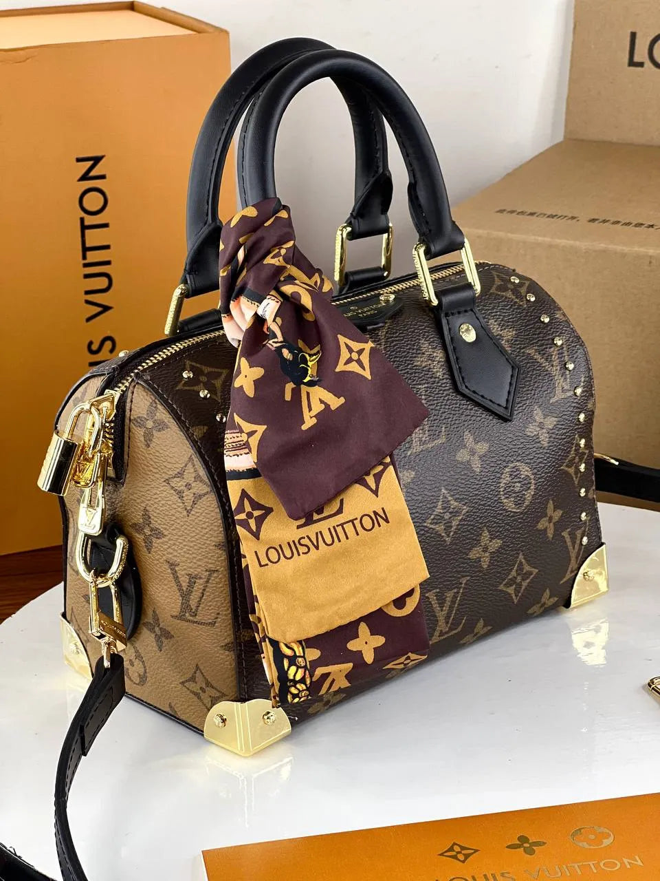 Louis Vuitton handbag with monogram pattern and matching scarf on a white surface with branded boxes in the background.