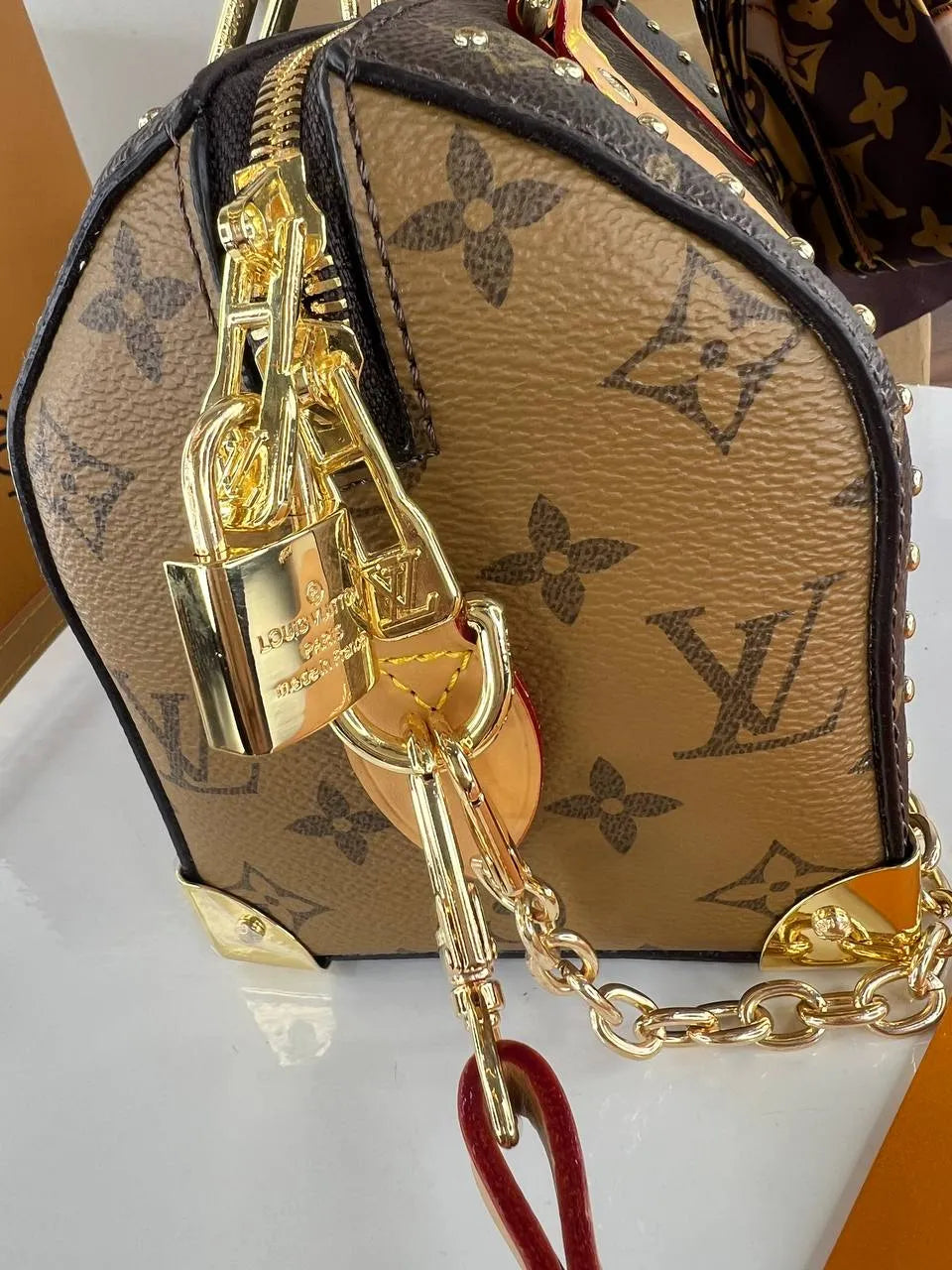 Designer handbag with gold chain and red strap on a white surface
