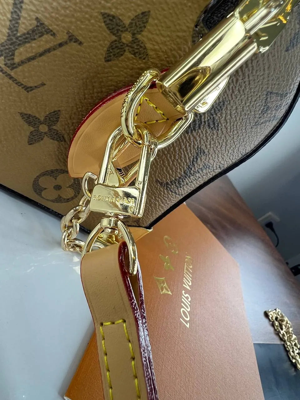 Gold chain keychain with Louis Vuitton logo on a patterned surface