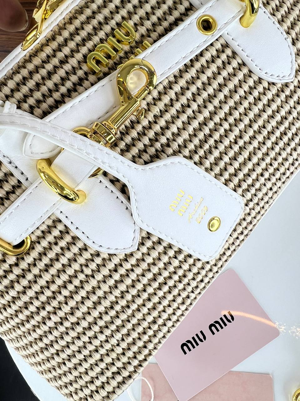 Close-up of a woven handbag with gold accents and 'Miu Miu' branding.