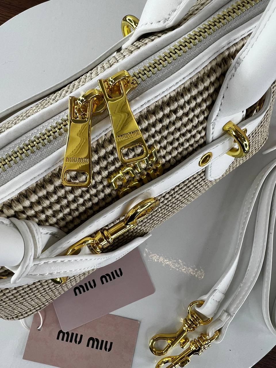 White handbag with gold zippers and Miu Miu tags on a white background