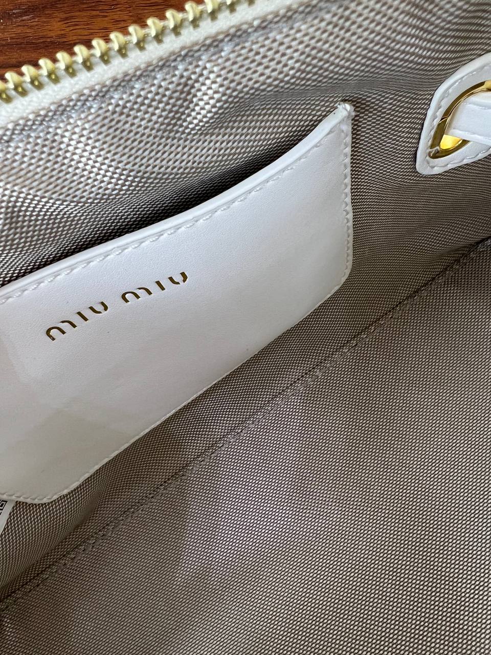 Close-up of a beige handbag with 'miu miu' branding on a wooden surface.