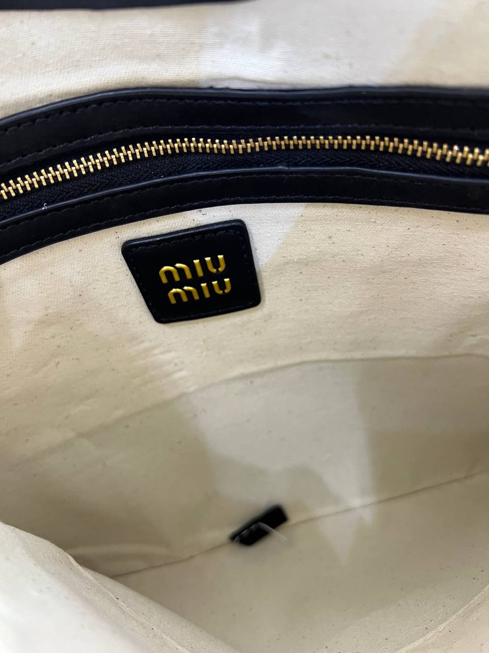 Close-up of a beige handbag with a gold zipper and Miu Miu logo.