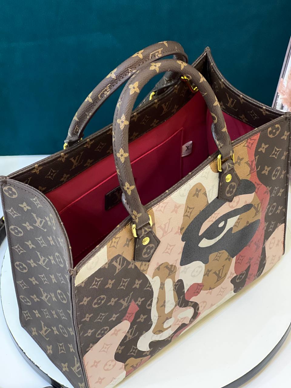 Designer handbag with artistic design and monogram pattern on a white surface.