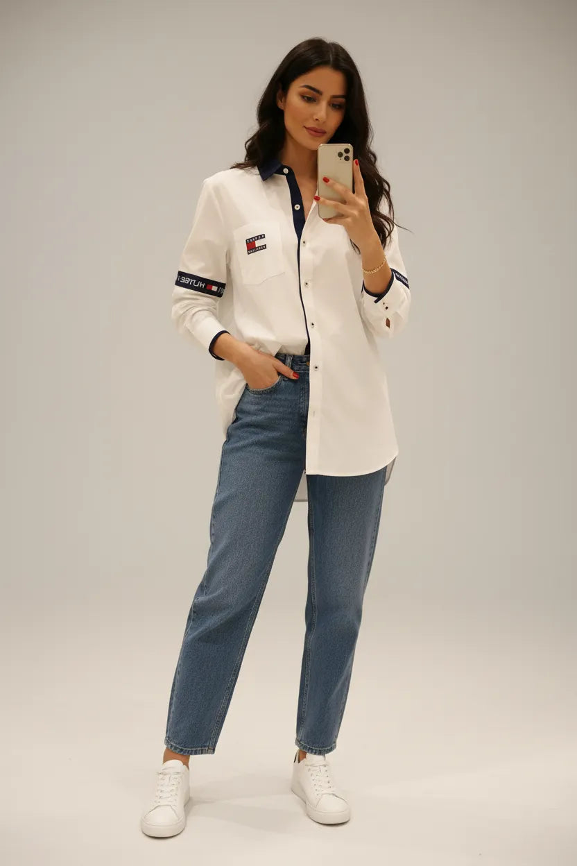Female model wearing Tommy Hilfiger white relaxed fit shirt blue relaxed jeans white sneakers light gray studio background