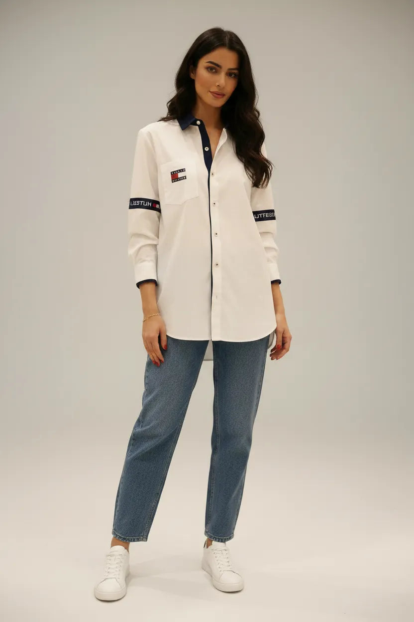 Female model wearing Tommy Hilfiger white relaxed fit shirt blue relaxed jeans white sneakers light gray studio background