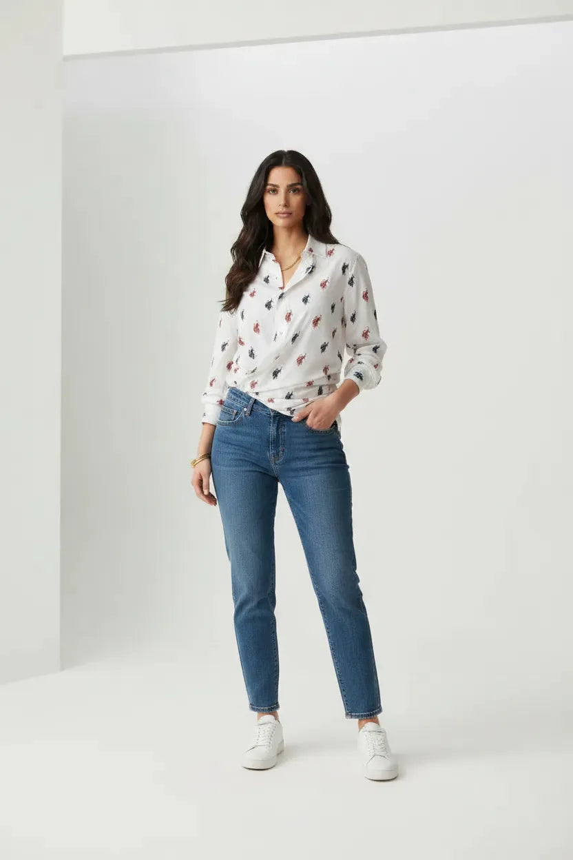 Female model wearing U.S. Polo Assn. white equestrian print shirt with blue tapered jeans and white sneakers