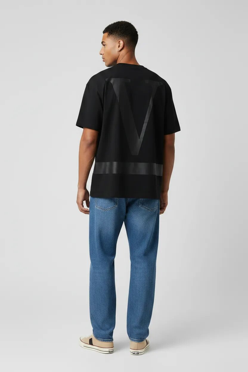 Man wearing a black t-shirt with a logo and blue jeans on a white background