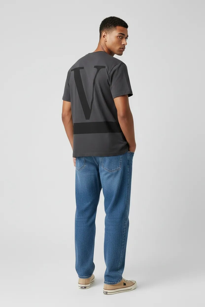 Man wearing a gray t-shirt with a logo and blue jeans on a white background
