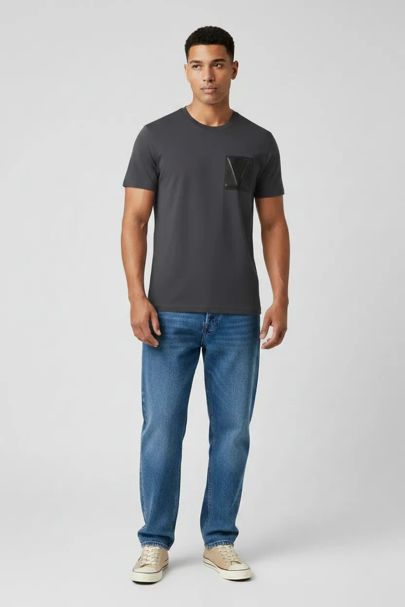 Man wearing a dark gray t-shirt with a pocket and blue jeans on a light gray background